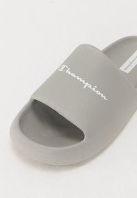 Grå slidesandal laget av myk gummi med åpen tå-design. Har en teksturert overflate og hvit "Champion"-logo på den øvre stroppen.