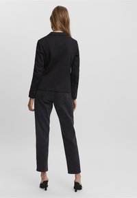 Černý blazer s přiléhavým střihem a klopami, v kombinaci s tmavě šedými rovnými džíny. Hladká textura a jednoduché knoflíkové detaily.