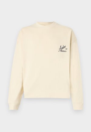 Crème-kleurige sweatshirt gemaakt van zachte stof, met een ronde halslijn en een klein zwart logo op de linkerborst. Ribbelboorden aan de mouwen en onderkant.