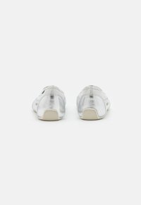 Scarpe metalliche argento con tomaia liscia, punta arrotondata e suole in gomma. La vista posteriore rivela una texture morbida e un design minimalista.