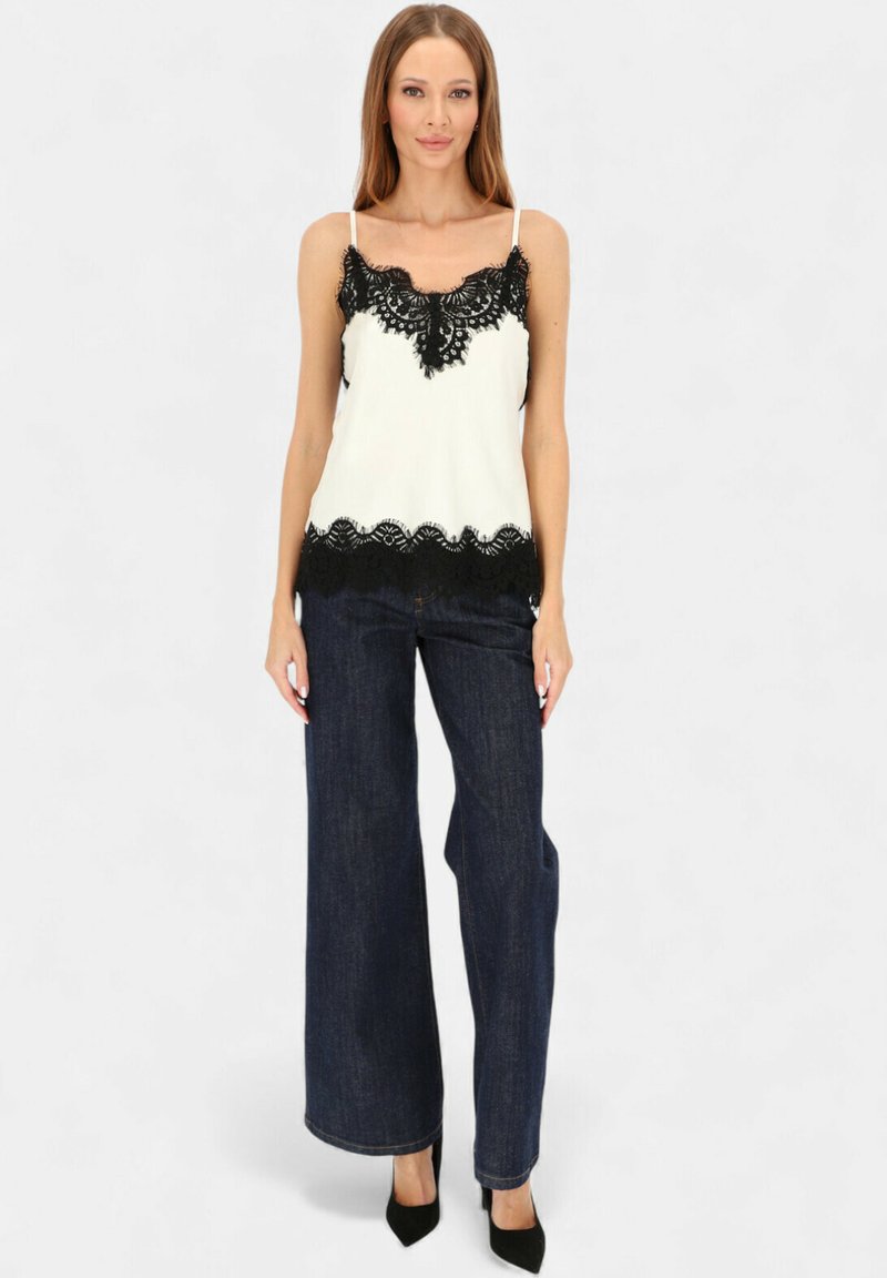 Biały top na cienkich ramiączkach z czarną koronkową lamówką, zestawiony z ciemnymi dżinsami o szerokich nogawkach i czarnymi szpilkami. Gładka tkanina, elegancki fason.