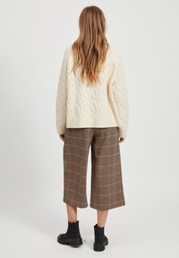 Pull en maille torsadée crème, culottes à carreaux marron, et bottines noires. Mettez l'accent sur les textures et les motifs de la tenue.