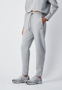 Pantaloni tuta grigi realizzati in un morbido tessuto testurizzato, con cintura regolabile, tasche laterali e gambe taperate, abbinati a scarpe sportive grigie.