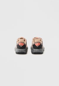 Sport shoes with a beige mesh upper, black accents, and a textured sole. Features prominent red logos on the heel and a cushioned collar.