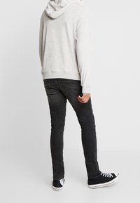 Sudadera gris con capucha, puños y dobladillo acanalados, combinada con jeans negros ajustados y zapatillas negras con suelas blancas.