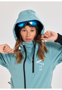 Lichtblauwe skijas met een hoge kraag en verstelbare capuchon. Heeft zwarte ritsen, een wit logo en een zachte binnenvoering. Bevat skibril.