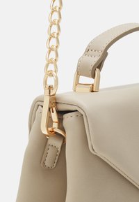 Beige kunstlædertaske med tekstureret finish, der har en guldfarvet kædestropp og spænde, som er fastgjort til et struktureret klaplåg design.