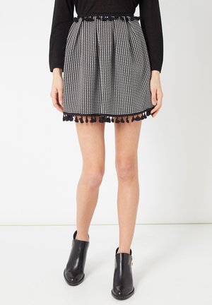 Falda a cuadros en blanco y negro con un diseño acampanado, que presenta una tela texturizada y un borde con flecos negros en el dobladillo. Combinada con botas de tobillo.