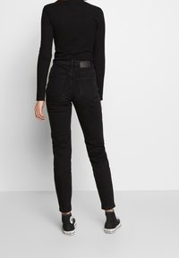 Jeans negros elásticos con corte ajustado, que cuentan con una cintura alta, diseño de cinco bolsillos y un ligero desgaste. Combinados con botas negras de tobillo.