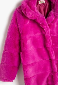 Cappotto in pelliccia sintetica di un brillante colore rosa, dotato di cappuccio, chiusura con bottoni e texture trapuntata. Le maniche sono leggermente oversize. Materiale morbido e soffice.