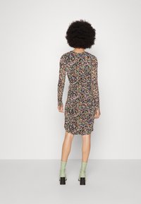 Vestido de manga larga, ajustado, en negro con estampado floral multicolor; diseño fruncido; a la altura de la rodilla; combinado con botas de tacón en verde claro.