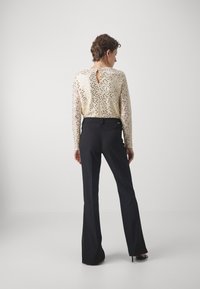 Top lungo a maniche con paillettes dorate metallizzate e dettaglio a chiave sulla schiena, abbinato a pantaloni neri a zampa e scarpe con tacco nere.