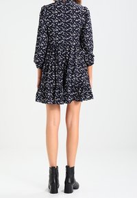 Marinblå blommig klänning med långa ärmar, utsvängd nederdel och volangdetaljer. Matchad med svarta ankelstövlar. Har ett litet blommönster.