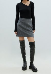 Schwarzes Langarmshirt, grauer Minirock mit Nadelstreifen und knielange schwarze Lederstiefel mit derben Sohlen. Einfaches, tailliertes Design.
