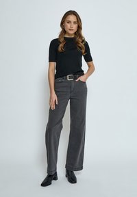 Top negro de manga corta combinado con unos pantalones vaqueros de tiro alto y holgados de color gris oscuro. Completa el look con unas botas negras de tobillo y un cinturón de hebilla plateada.