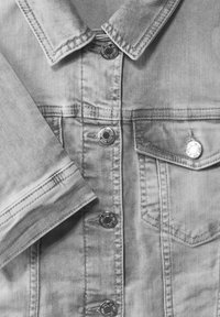 Šedá džínová bunda s kovovými stříbrnými knoflíky, špičatým límcem a předními kapsami. Měkká textura s jemným vyblednutím a prošitými detaily.