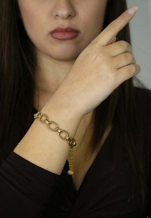Goldenes Armband mit runden Gliedern und texturierten Details, getragen am Handgelenk. Das Design umfasst eine Kettenerweiterung und einen kleinen Anhänger.