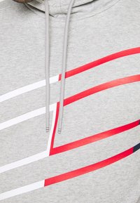 Felpa grigia con grafiche lineari rosse e bianche. Stringhe di chiusura in grigio abbinato con punte argentate. Tessuto morbido con vestibilità casual.