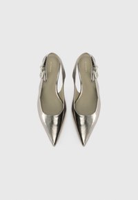 Metallic sølv slingback pumps med spidse tæer og udskæringsdesign. Har en dekorativ spændeaccent på hælen. Glat tekstur.