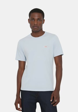 T-shirt azzurro chiaro a maniche corte in un tessuto morbido, con un piccolo logo rosso sulla parte sinistra del petto. Design semplice con collo rotondo.