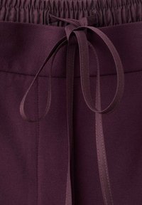 Dieprode stof met een gestructureerd oppervlak; beschikt over een elastische tailleband met een bijpassende lintstrik. Eenvoudige en functionele ontwerpdetails.