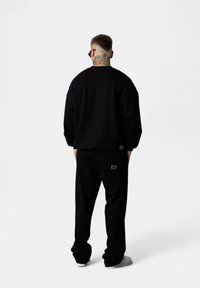 Sweatshirt et pantalon noirs en tissu doux, avec une coupe décontractée et un design minimaliste. Petit détail de logo sur la poche du pantalon.
