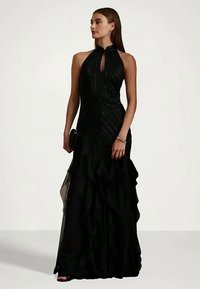 Čierne šaty bez rukávov s priliehavým vrchom, textúrovanými detailmi a vrstveným volánom na lemovaní. Spárované s malou čiernou kabelkou.