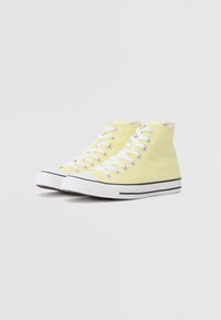 Hochschuh-Sneaker aus leuchtend gelbem Canvas mit weißen Schnürsenkeln, schwarzen Streifen entlang der Sohle und einer Gummizunge.