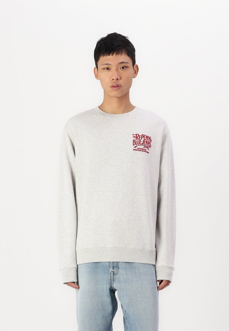 Sudadera gris clara con cuello redondo y mangas largas. Presenta un logo rojo en el pecho y puños y dobladillo acanalados.