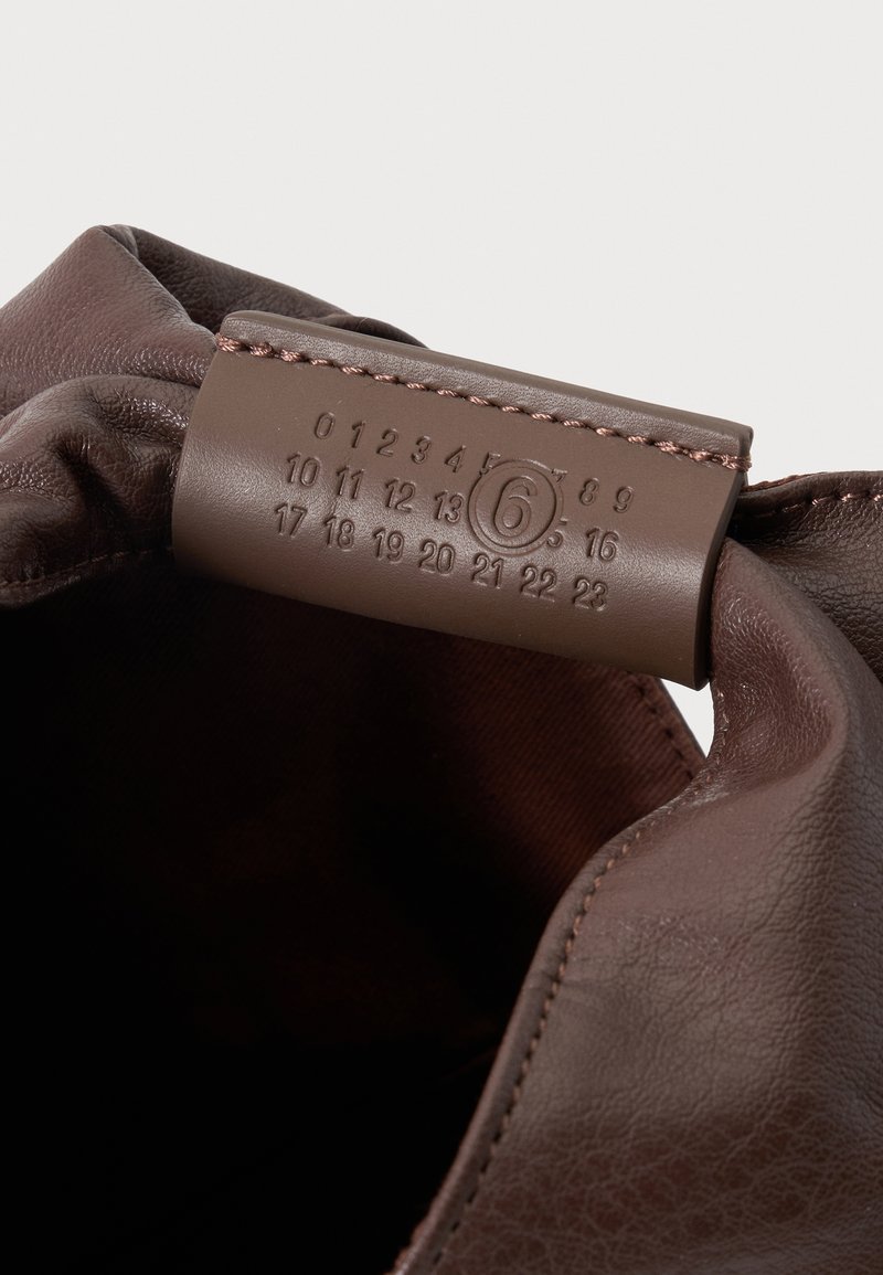 Sac en cuir marron avec étiquette cousue montrant les numéros de 0 à 23, avec le numéro 6 entouré, à l'intérieur de l'ouverture du sac.
