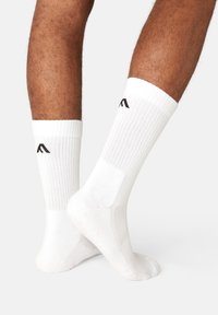 White cotton socks featuring ribbed texture, reinforced heel and toe, with a black logo on the cuff.