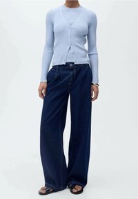 Cárdigan de canalé azul claro con escote en V y botones, combinado con pantalones de mezclilla de pierna ancha azul oscuro y sandalias planas negras.