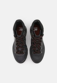 Svarta vandringsskor med texturerad läderövre del, röda och svarta snören, metallöglor och vadderad krage. Förstärkt tåhätta för hållbarhet.