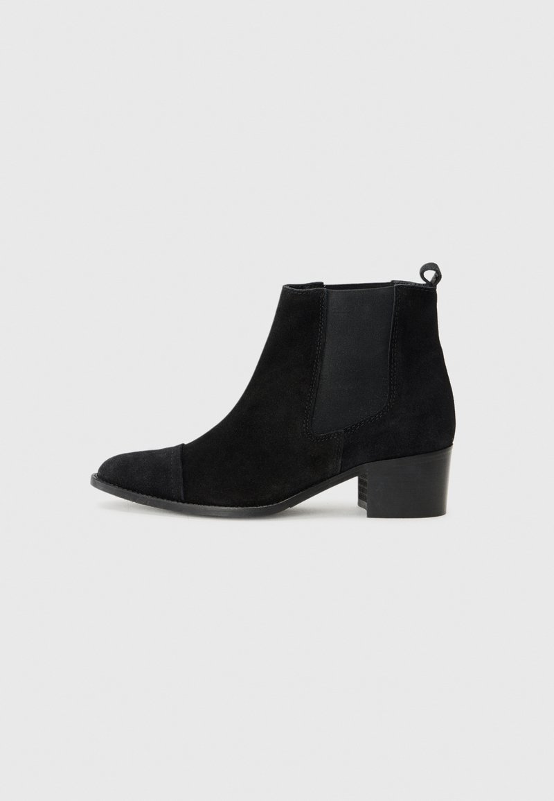 Bottine noire en daim avec talon bloc bas, panneaux latéraux élastiques et languette à l'arrière sur fond gris clair.
