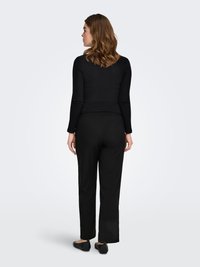 Musta ribbineuloksinen pitkähiha top yhdistettynä mustiin väljälahkeisiin housuihin. Näkyvissä tasapohjaiset mustat kengät. Yksinkertainen ja minimalistinen muotoilu.