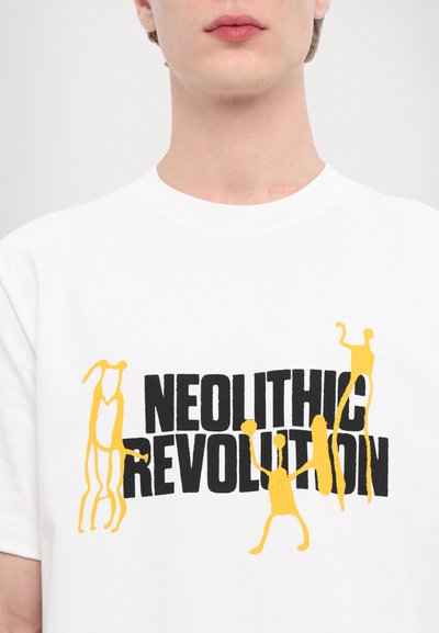Tricou alb din bumbac cu un grafic îndrăzneț în negru al textului „REVOLUȚIA NEOLITICĂ” și figuri abstracte galbene. Textură netedă.