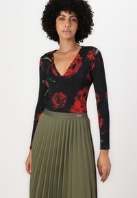 Body nero con stampa di rose rosse, scollatura a V profonda, maniche lunghe; abbinato a una gonna plissettata verde oliva con logo in vita.