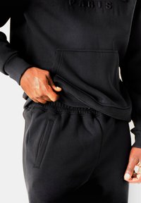 Felpa nera con logo "PARIS" in rilievo e tasca a marsupio, abbinata a pantaloni jogger neri coordinati con vita elastica e tasca laterale.