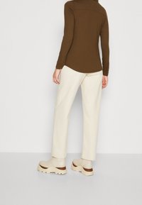 Top marrón de manga larga con dobladillo redondeado, combinado con pantalones anchos de color crema y zapatos de plataforma beige con detalles en marrón.