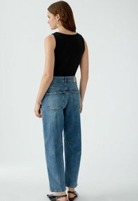 Schwarzes ribbeliges ärmelloses Oberteil kombiniert mit hochtaillierten hellblauen Jeans, die einen geraden Schnitt und zwei Gesäßtaschen haben.