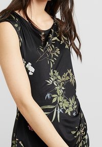 Czarna sukienka z kwiatowym wzorem w odcieniach zieleni, bieli i niebieskiego. Posiada okrągły dekolt, krótkie rękawy oraz marszczenia po bokach.