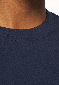 Marinblå bomull t-shirt med rund hals, korta ärmar och en slät textur. Sömmen syns runt kragen.