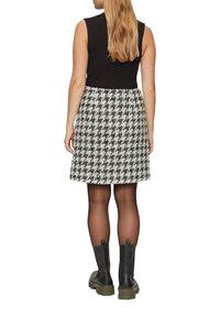 Schwarzes geripptes, ärmelloses Oberteil, kombiniert mit einem grauen Hahnentrittmuster-Rock mit Schlag. Das Modell trägt schwarze klobige Stiefel mit grünen Sohlen.