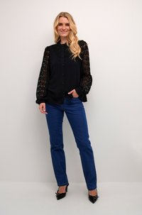 Svart knapp-up blus med spetsärmar, kombinerad med blå denimjeans och svarta spetsiga klackskor. Slätt tyg med texturerade accenter.