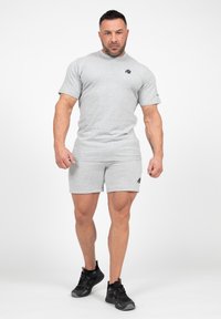 Grijs sport T-shirt en korte broek van een katoenmix; heeft een klein zwart logo op de borst en aan de zijkant, gecombineerd met zwarte sneakers.