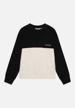 Długi sweter z długim rękawem w kolorach czarnym i beżowym, z logo Calvin Klein na czarnej górnej części klatki piersiowej.