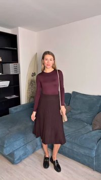Pikad varrukad burgundia tooniga topp, millele on kombineeritud must plisseeritud midi-seelik. Mustad loafersid ja väike beež ristiülekande kott. Heledat tausta koos mööbliga.