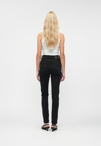 Fekete magas derekú farmernadrág, slim fit fazonnal, öltött hátzsebekkel és texturált anyaggal, fehér ujjatlan topmal és fekete magassarkúval párosítva.