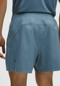 Miesten urheilushortsit vaaleansiniset, valmistettu sileästä, kevyestä kankaasta. Ominaisuuksiin kuuluu joustava vyötärönauha ja hillitty logon yksityiskohta sivulla.