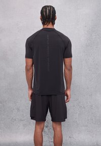Camiseta deportiva negra de manga corta, hecha de material ligero. Presenta un logo impreso verticalmente en la parte posterior. Combinada con pantalones cortos a juego.